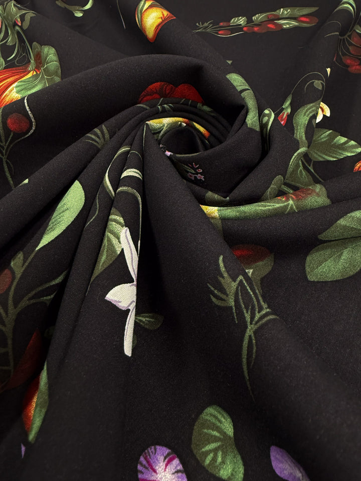 A close-up of Super Cheap Fabrics' Designer Rayon - Dark Orchard Bloom (145cm), showcasing its vibrant floral and leaf pattern and smooth, lightweight texture twisted into a spiral.