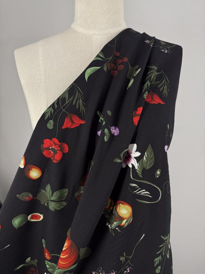 A mannequin displays Super Cheap Fabrics’ Designer Rayon - Dark Orchard Bloom (145cm), a lightweight rayon with a vibrant floral and fruit print in red, green, and purple, draped diagonally across the shoulder.