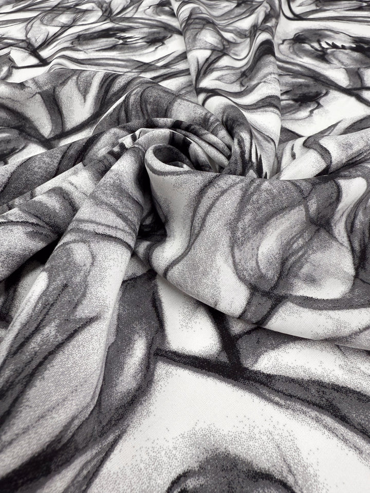 A close-up of Super Cheap Fabrics' Designer Rayon - Shadow Petal (148cm), showing its lightweight black and white abstract swirl pattern, loosely gathered to highlight elegant folds and shadows.