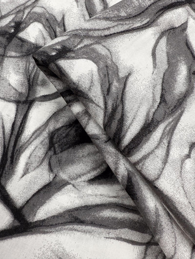 A close-up of Super Cheap Fabrics’ Designer Rayon - Shadow Petal (148cm), showing two overlapping pieces with a black and gray abstract floral print on white, featuring soft, flowing lines for a textured look.