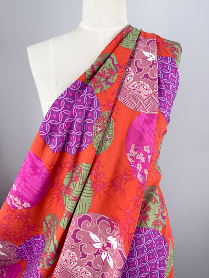 A mannequin displays Super Cheap Fabrics' Designer Rayon - Kyoto Lanterns (146cm), featuring bright orange fabric with circular patterns in purple, pink, and green. The plain background is light gray.