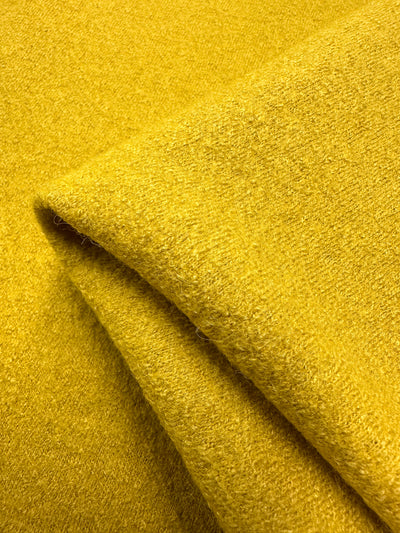 Close-up of folded mustard yellow Boiled Wool - Hot Spot by Super Cheap Fabrics, 145cm wide. This heavyweight wool-viscose blend has a soft, textured surface that looks cozy and warm, with its plush texture capturing light.