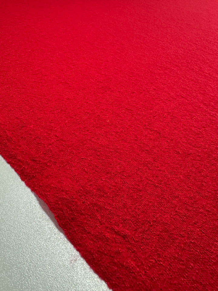 The vibrant Boiled Wool in Racing Red from Super Cheap Fabrics, 145cm wide, features a textured surface with sharp contrast against a smooth gray floor, highlighting the difference in texture and color.