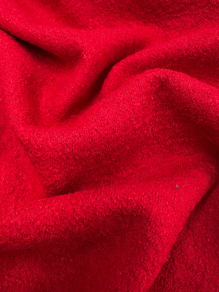 A close-up of Super Cheap Fabrics' Boiled Wool in Racing Red (145cm) reveals its soft, textured appearance. The heavy fabric drapes and folds elegantly, casting gentle shadows and highlights reminiscent of cozy winter garments.