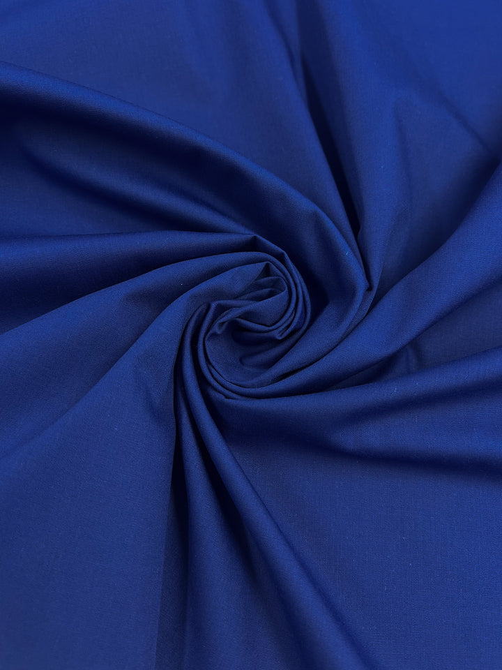 A close-up of Super Cheap Fabrics' Poplin - Bluing - 148cm reveals a spiral pattern in a lightweight polyester cotton blend, giving an impression of movement and texture with a smooth and slightly shiny surface that subtly reflects light.