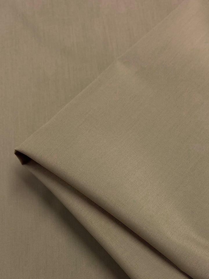 A folded piece of olive green fabric, Poplin - Safari - 148cm by Super Cheap Fabrics, rests on a flat surface. Soft lighting accentuates its smooth texture, highlighting the lightweight polyester-cotton blend’s refined appearance that's perfect for crafting garments.