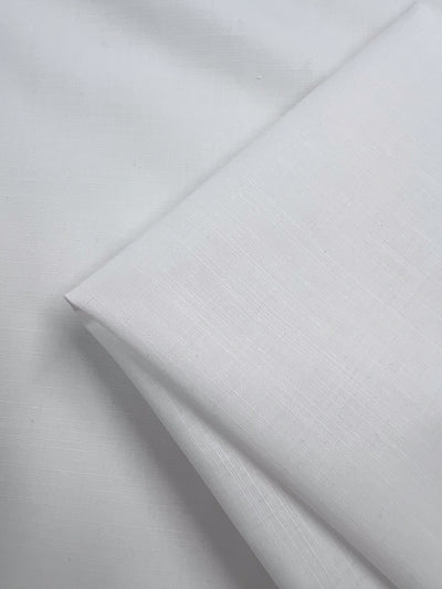 Close-up of neatly folded Poplin - White - 148cm by Super Cheap Fabrics, ideal for childrenswear. The fabric looks smooth with subtle textures, indicating a fine weave, while the lighting highlights its clean, crisp appearance and lightweight feel.