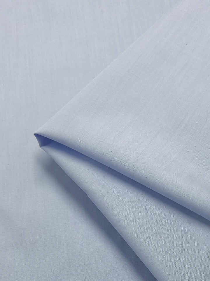 Close-up of Super Cheap Fabrics' Poplin - Ancient Water - 148cm, featuring a light blue color with a smooth texture and soft sheen. The fine polyester cotton blend weave indicates its high quality.