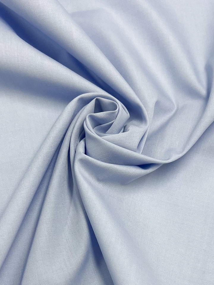 A close-up of Super Cheap Fabrics' "Poplin - Ancient Water - 148cm" reveals a light blue, non-stretch fabric with a swirling pattern and subtle sheen, evoking softness and smoothness akin to a polyester cotton blend.