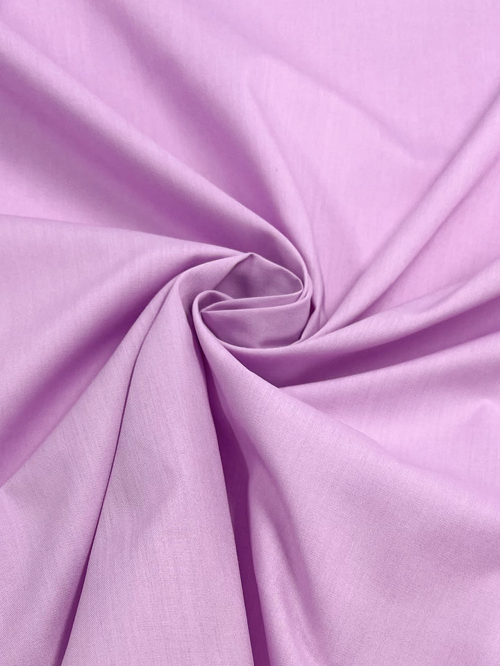 A close-up of Super Cheap Fabrics' Poplin in Pastel Lavender - 148cm features a swirl of light purple polyester-cotton blend, with smooth folds forming a gentle, textured look.