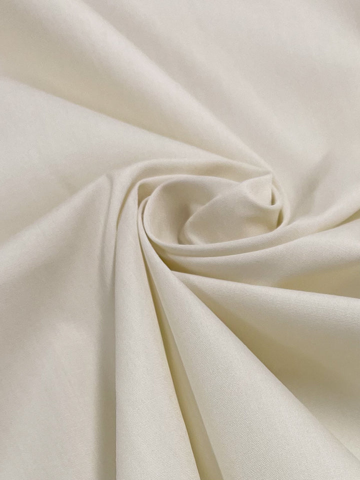 A close-up of Poplin - Snow White from Super Cheap Fabrics, featuring light cream-colored polyester cotton blend with a smooth texture, artistically spiraled to create soft folds and curves.