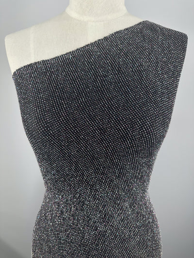 A mannequin showcases a one-shoulder dress crafted from Super Cheap Fabrics' Metallic Lycra - Disco 150cm. The textured black fabric with a sparkling silver pattern stands out against a neutral gray background, enhancing the elegance of these stunning dresses.