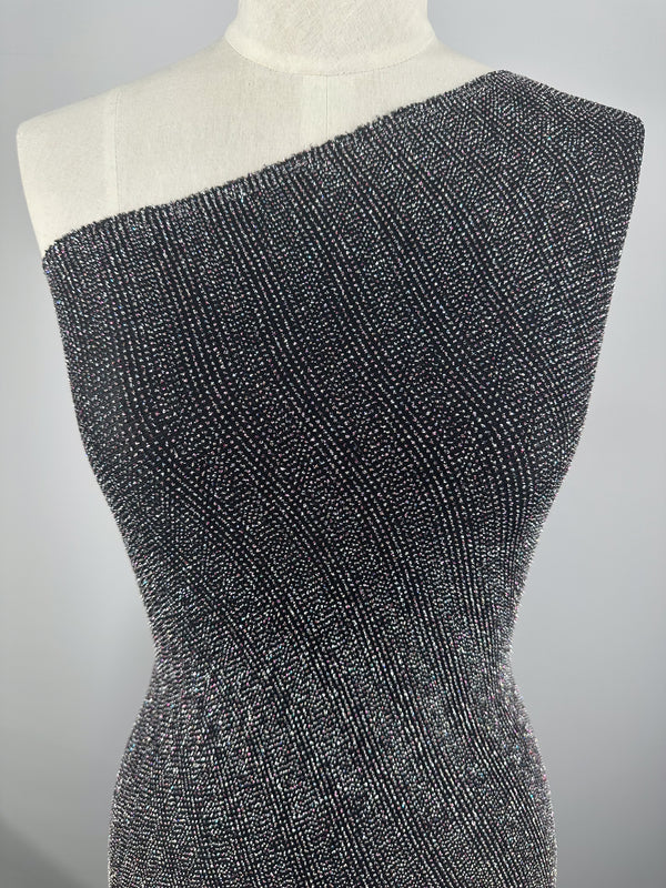 A mannequin showcases a one-shoulder dress crafted from Super Cheap Fabrics' Metallic Lycra - Disco 150cm. The textured black fabric with a sparkling silver pattern stands out against a neutral gray background, enhancing the elegance of these stunning dresses.