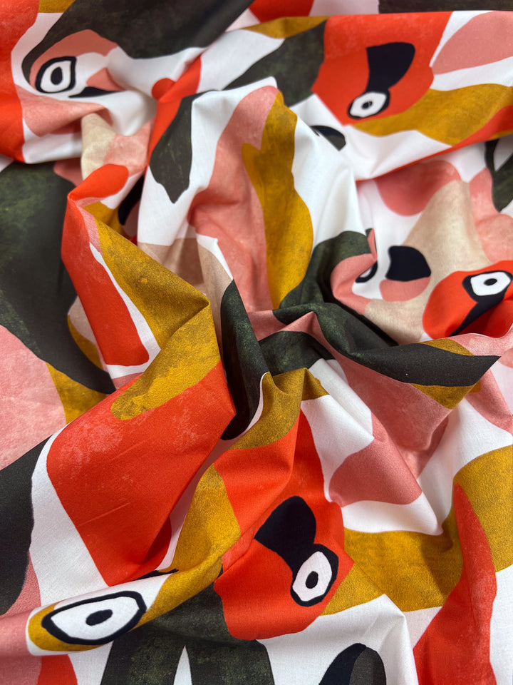 The "Printed Cotton - Tucan - 150cm" by Super Cheap Fabrics is a lively, lightweight fabric featuring abstract red, orange, black, green, and white patterns for an artistic look. The slightly crumpled natural cotton fibers enhance its texture and depth.