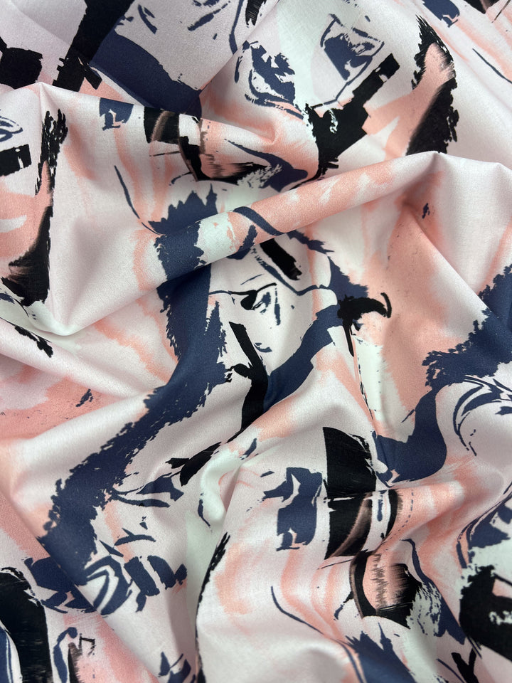 A close-up of the lightweight Printed Cotton - Peaches & Cream (150cm) by Super Cheap Fabrics showcases its pink, black, and white abstract patterns with bold brush-like strokes and swirls. The slightly crumpled natural cotton fibers add texture to this dynamic, artistic fabric.