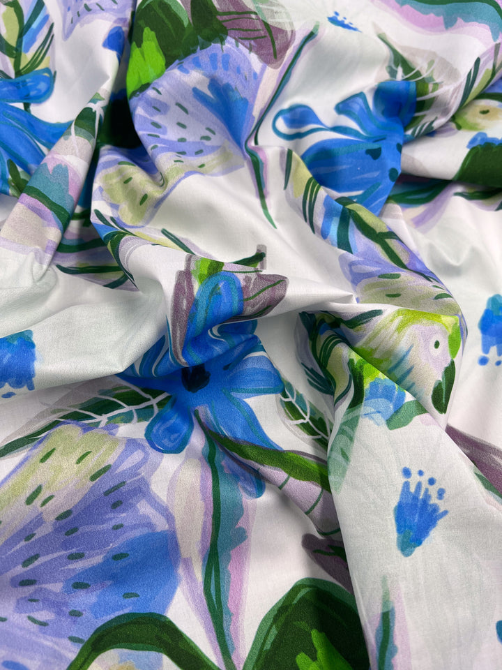 A close-up of crumpled, lightweight Super Cheap Fabrics' Printed Cotton - Blue Paradise, showcasing large blue flowers and green leaves on a white background for a lively and colorful appearance with natural fibers. Width: 150cm.