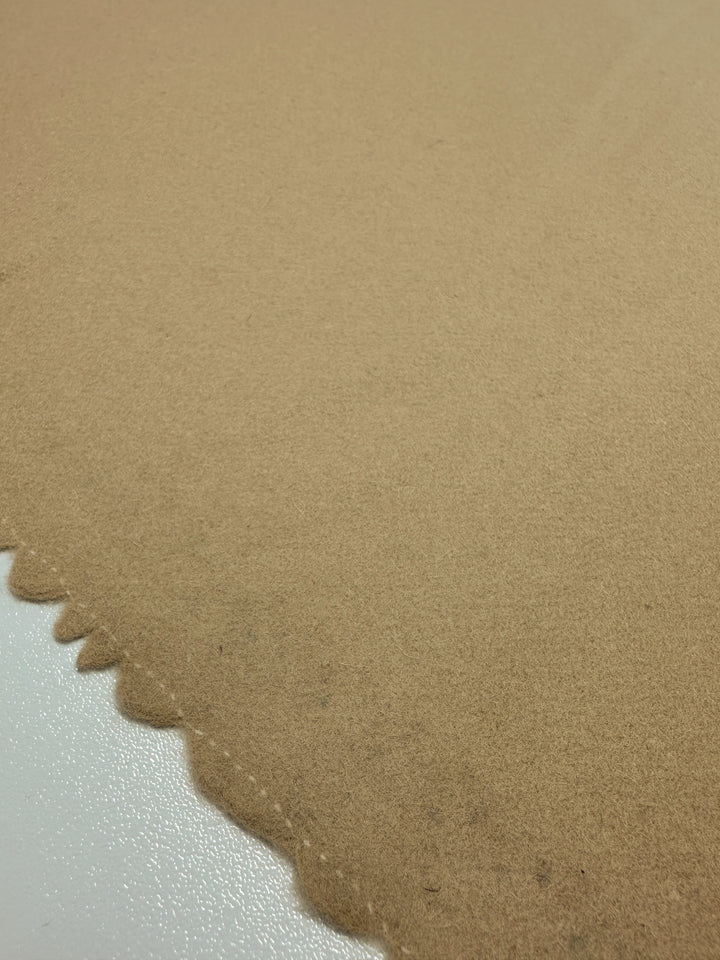 A close-up of Super Cheap Fabrics' luxurious Merino Wool - Curd & Whey, 150cm, reveals its soft, tan-colored surface with a scalloped edge against a reflective white background.