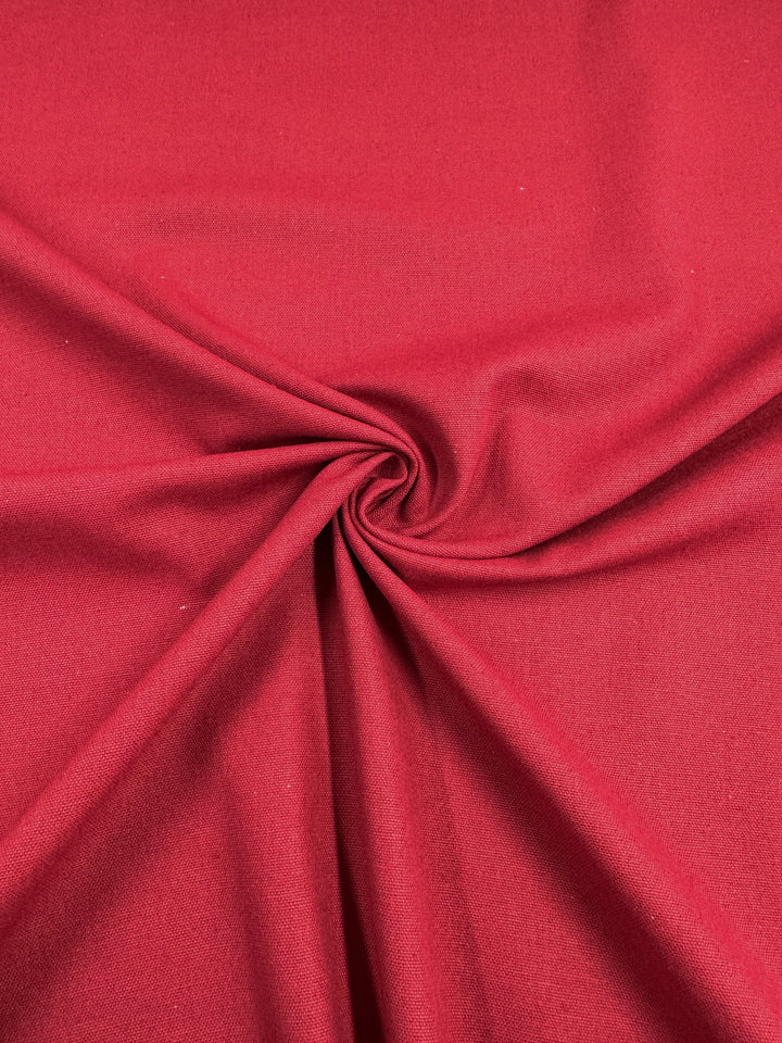 A close-up view of a piece of Super Cheap Fabrics' Linen Blend - Salsa - 150cm with a prominent swirl pattern in the center, creating folds radiating outward. The medium weight linen texture appears smooth, with a deep and rich color.