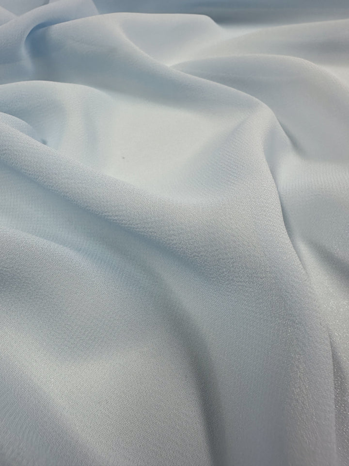 The Hi-Multi Chiffon in Powder Blue by Super Cheap Fabrics is a smooth, slightly shimmery fabric that drapes delicately, creating gentle folds with subtle shadows and a textured surface—ideal for crafting ethereal floaty tops. Width: 150cm.