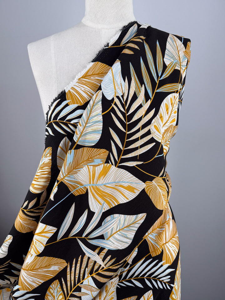 A mannequin displays Super Cheap Fabrics’ Bamboo Rayon - Tropic Gold (150cm): a lightweight fabric with bold gold, white, and light blue tropical leaves on gray—perfect for beginner-friendly sewing projects.