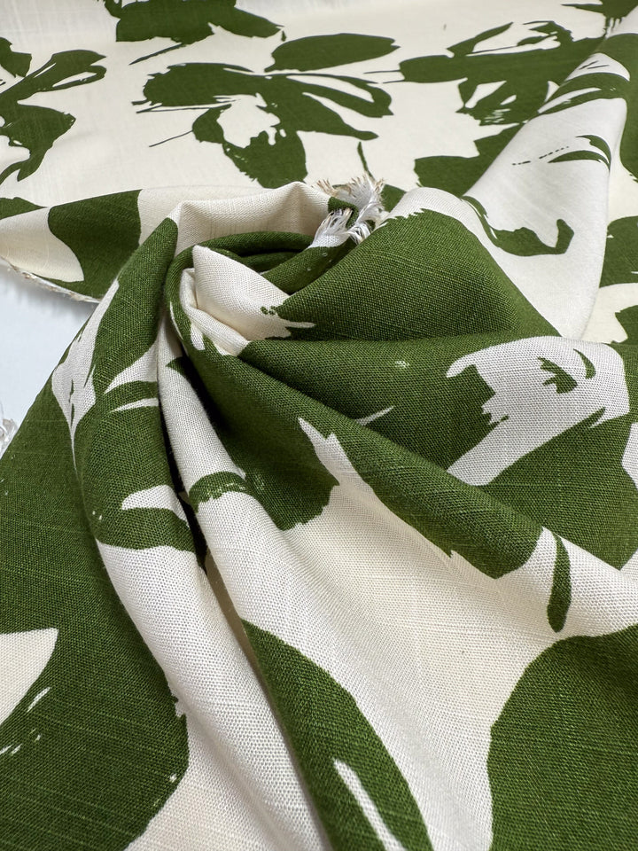 A close-up of Super Cheap Fabrics' Bamboo Rayon - Olive Bloom - 150cm, featuring cream fabric with green botanical prints, loosely folded with subtle fraying that highlights its lightweight, beginner-friendly texture and pattern.