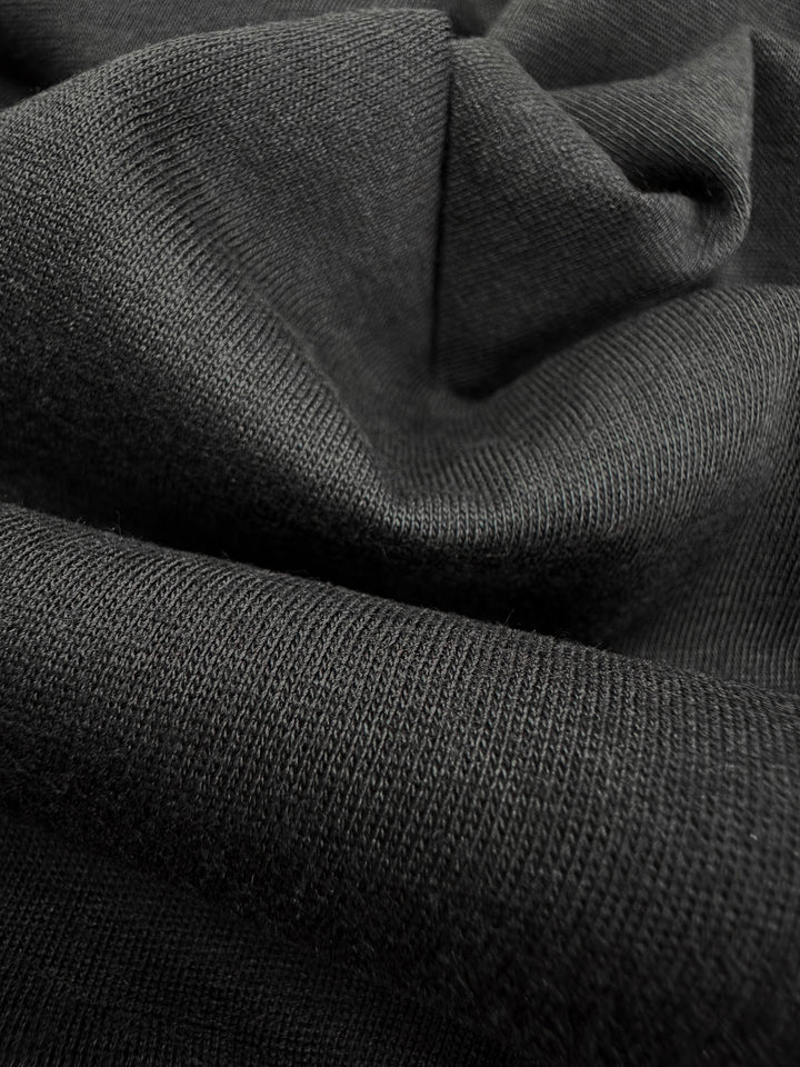 Close-up of the Lightweight Cotton Jersey by Super Cheap Fabrics in Black (145cm). The jersey features a textured, knitted pattern and appears soft and slightly crumpled, showcasing its flexibility and thickness.