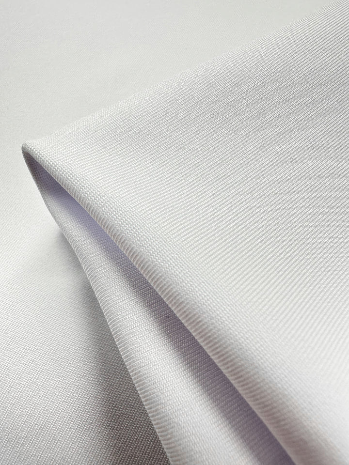 A close-up of a neatly folded piece of Plain Lycra - Snow White, 160cm by Super Cheap Fabrics, reveals its smooth and lightweight appearance. The subtle textured fabric epitomizes a soft, minimalistic aesthetic ideal for activewear.