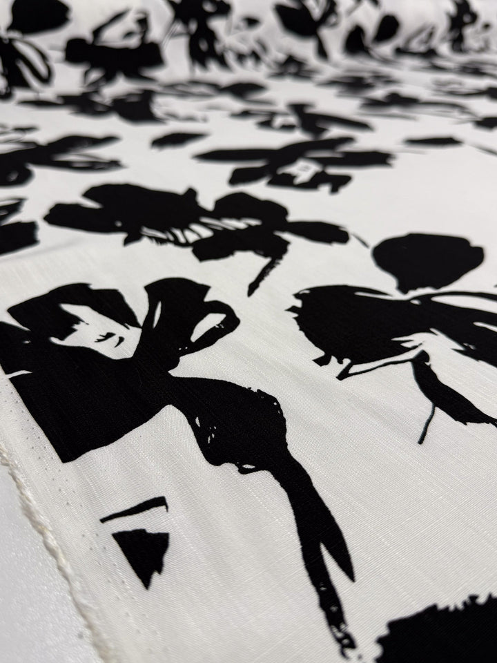 A close-up of Super Cheap Fabrics' Bamboo Rayon - Jet Bloom (150cm) shows its lightweight feel and bold, abstract black floral pattern scattered across the surface—perfect for beginner-friendly sewing projects.