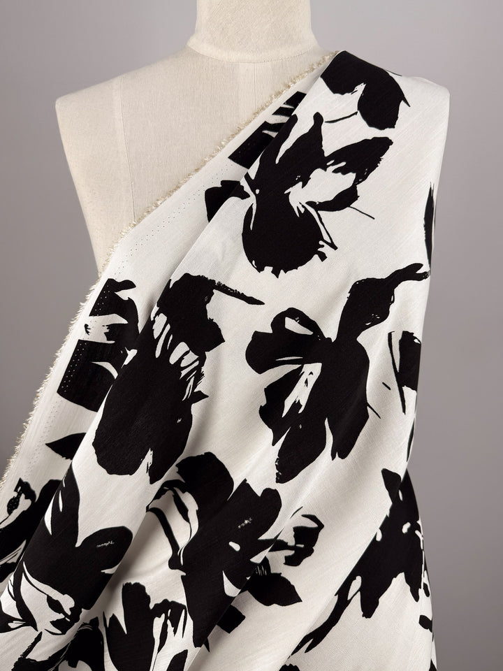 Super Cheap Fabrics' Bamboo Rayon - Jet Bloom (150cm) is shown draped on a white dress form with a bold, black abstract floral print on white. Ideal for beginner sewing projects, the fabric is displayed diagonally against a neutral backdrop.