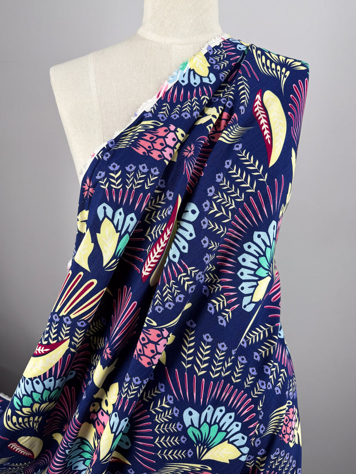 A dress form displays Super Cheap Fabrics’ Bamboo Rayon - Midnight Carnival (150cm), a dark blue fabric with vibrant yellow, pink, green, and blue floral and leaf patterns—perfect for beginner-friendly sewing projects.