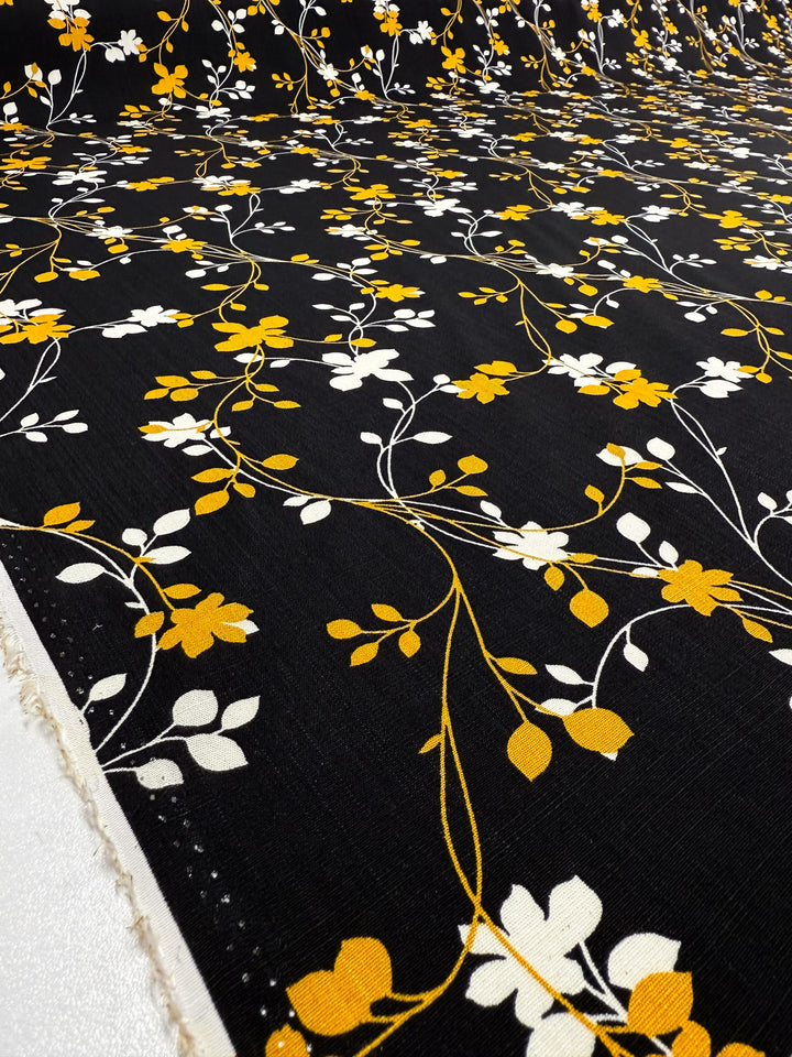 Super Cheap Fabrics' Bamboo Rayon - Golden Vine (150cm) features lightweight black rayon with a repeating yellow and white floral vine pattern spread across the surface.