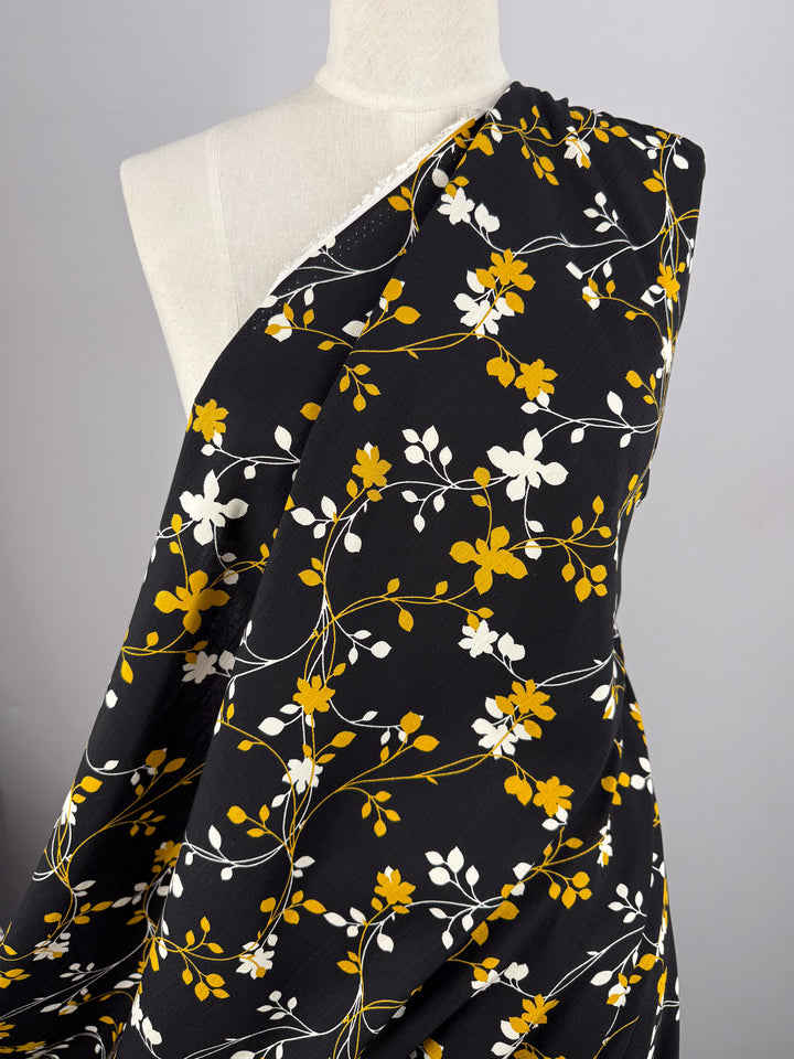 Super Cheap Fabrics' Bamboo Rayon - Golden Vine (150cm) is a lightweight black fabric with yellow, white, and orange floral and vine patterns—perfect for beginner-friendly sewing projects.
