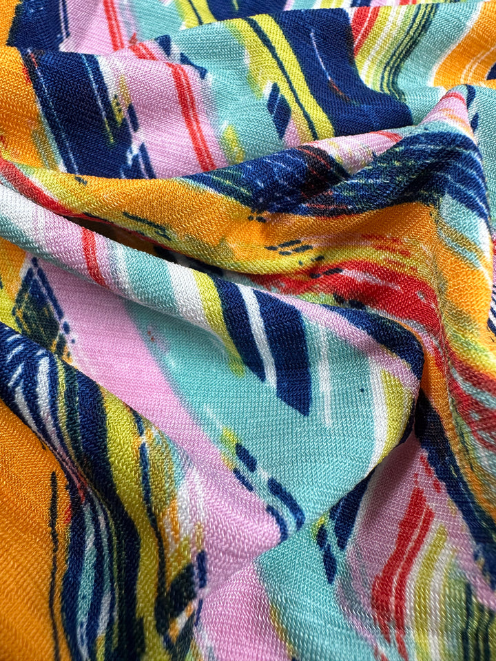 A close-up of the geo dome pattern on Printed Lycra from Super Cheap Fabrics illustrates its textured, vibrant abstract design with swirling lines in blue, yellow, pink, red, and green. This 145cm fabric is perfect for summer garments and highlights the rich colors and intricate weave beautifully.