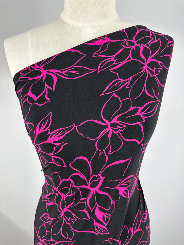 A mannequin features the "Printed Lycra - Devour - 145cm" dress from Super Cheap Fabrics, with a polyester/spandex blend and bold pink floral outlines on a black backdrop, offering comfortable two-way stretch for stylish ease.