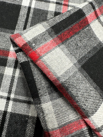 Close-up of a folded piece of Suiting - Tartanic - 147cm fabric from Super Cheap Fabrics. The pattern features a mix of black, white, grey, and red lines creating a classic tartan design. This lightweight fabric's texture appears soft and warm, making it a versatile fabric for various designs.