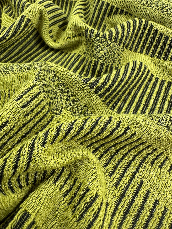 Close-up of Super Cheap Fabrics' Jacquard Knit - Chartreuse - 138cm displays textured green and black stripes. This fabric's intricate patterns and folds offer depth, complexity, and stretch for ultimate comfort.