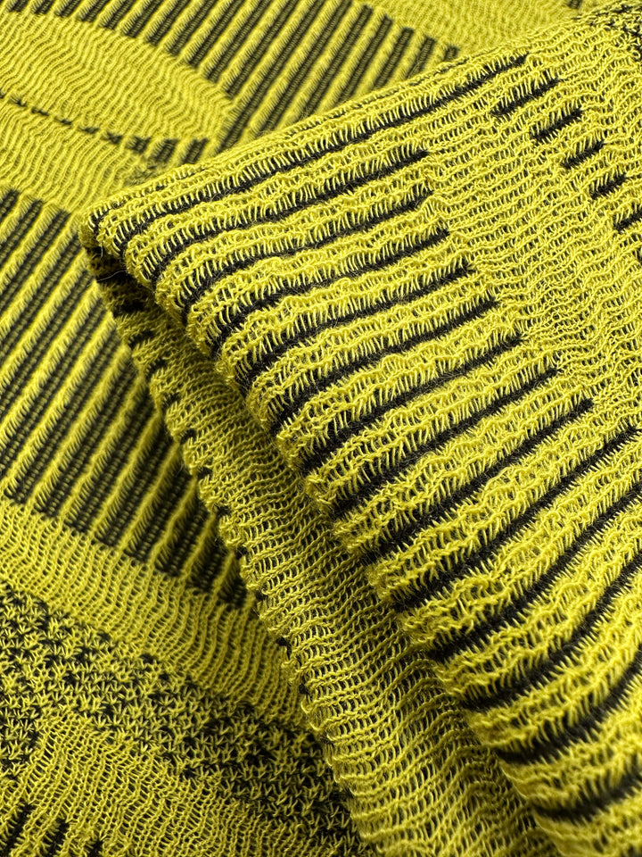 Detailed view of Jacquard Knit - Chartreuse by Super Cheap Fabrics: a folded yellow fabric with intricate black linear patterns, featuring knitted texture, contrasting stripes, and small circular shapes that offer stretch for maximum comfort. Width is 138cm.