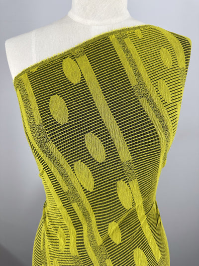 Draped over a mannequin, the Jacquard Knit - Chartreuse - 138cm fabric by Super Cheap Fabrics showcases black stripes with vertical lines and leaf-like designs in patterned yellow. Positioned against a plain gray background, its stylish stretch offers maximum comfort and elegance.