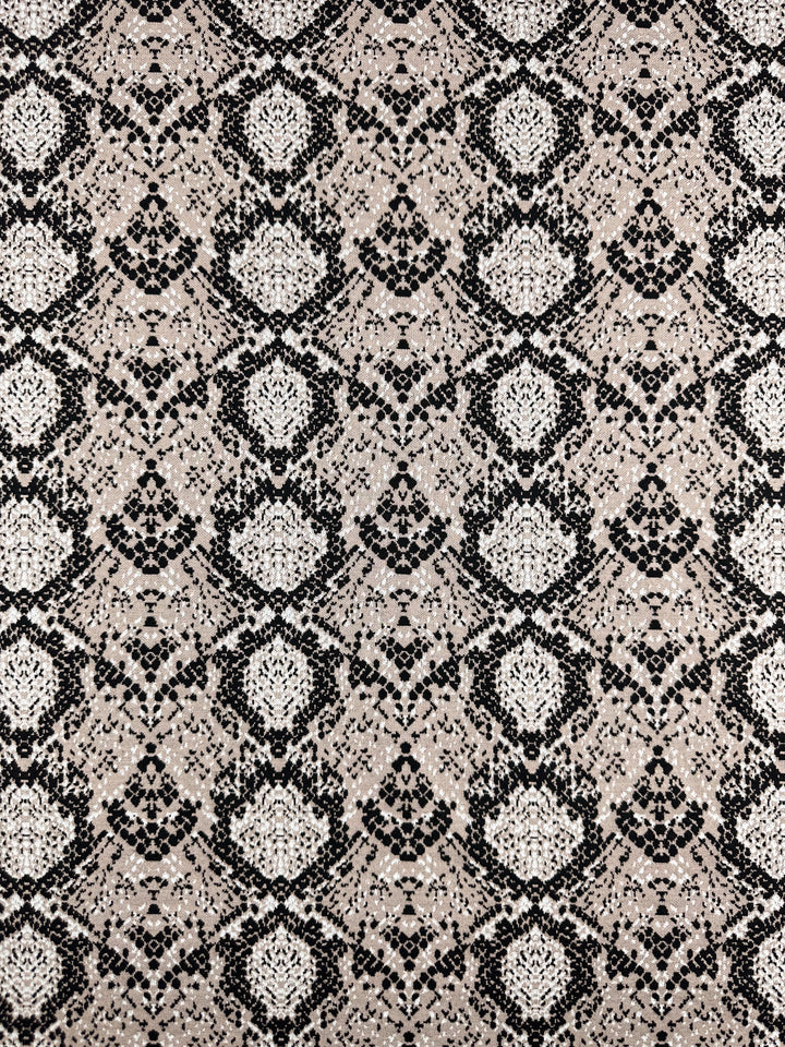 The Jacquard Knit - Mushroom fabric from Super Cheap Fabrics features a snakeskin-like symmetrical pattern of black and white geometric shapes on a beige backdrop, giving the medium-weight material an ornate, textured knit appearance. Width: 175cm.