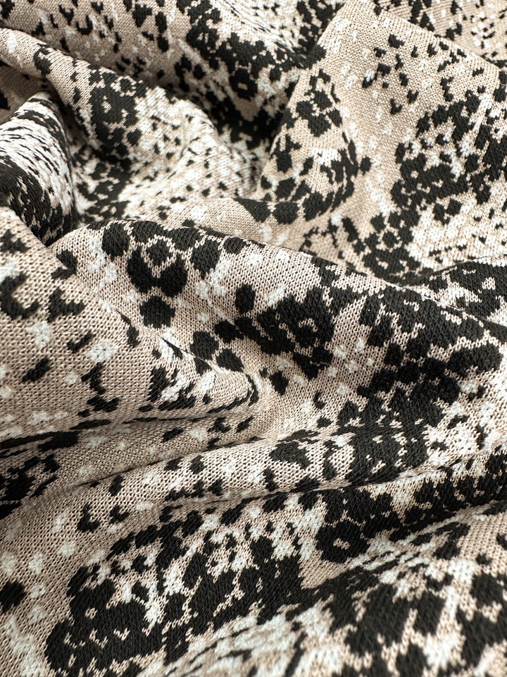 A close-up of a medium-weight Jacquard Knit in Mushroom by Super Cheap Fabrics showcases a textured, woven surface with intricate patterns and abstract organic shapes in beige, black, and white. Width: 175cm.