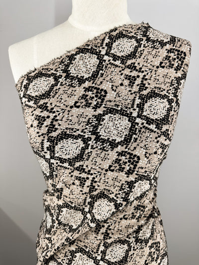 Close-up of a mannequin draped with Super Cheap Fabrics' Jacquard Knit - Mushroom (175cm). This medium-weight fabric features a black and beige snakeskin pattern, known for its generous stretch, styled asymmetrically over one shoulder to highlight its detailed texture and design.