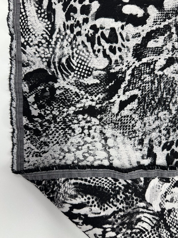 The "Survivor" Jacquard Bengaline by Super Cheap Fabrics is a 145cm medium-weight stretch fabric in black and white with an abstract animal print, featuring spot and scale-like patterns and neatly stitched gray edges.