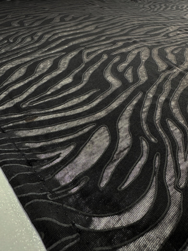 Detailed close-up of Super Cheap Fabrics' Burnout Jersey—Zebra, 160cm. The black-and-gray fabric features wavy zebra print patterns with glossy textures, showcasing its intricate design.