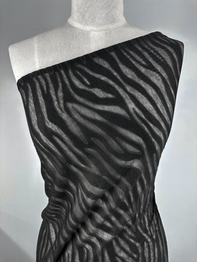 A mannequin displays a Super Cheap Fabrics' Burnout Jersey - Zebra, featuring wavy, abstract patterns similar to organic lines. The black fabric is elegantly draped over the shoulder against a plain gray background.