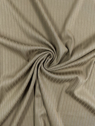 Close-up of the Super Cheap Fabrics' Rib Knit - Dune - 168cm, showcasing a medium weight beige fabric with a swirl pattern in the center. The material has a subtle sheen and vertical textured lines that create radiating folds.