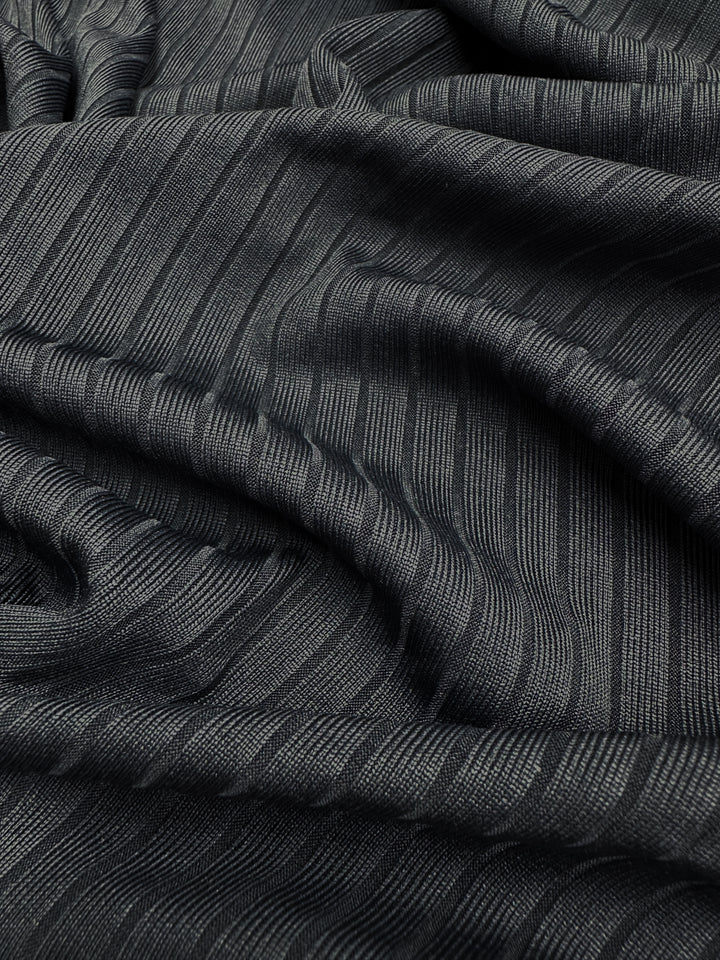 Close-up of a dark Rib Knit - Total Eclipse - 168cm fabric by Super Cheap Fabrics. This medium-weight textile showcases a textured, ribbed pattern draped in soft folds, highlighting its texture and subtle stretch typical of textured knits.