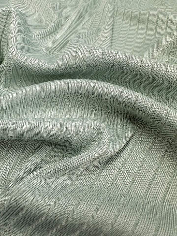 Close-up of Super Cheap Fabrics' Rib Knit - Murmur (175cm) in light green. This medium-weight fabric softly drapes with gentle folds and a subtle sheen, enhancing its elegant textured and flowing appearance.