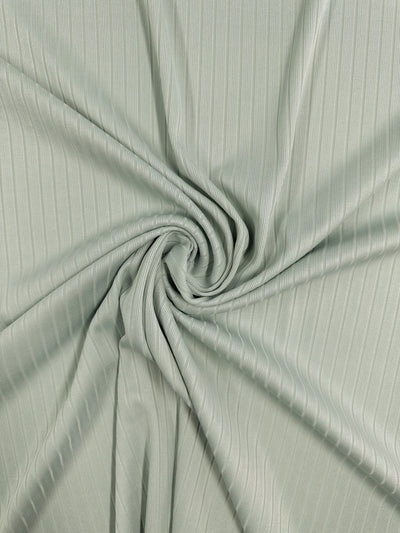 The Rib Knit - Murmur by Super Cheap Fabrics is a light green fabric with thin vertical lines, arranged in a spiral pattern at the center, creating soft folds and texture that showcase the allure of this medium-weight rib knit fabric.