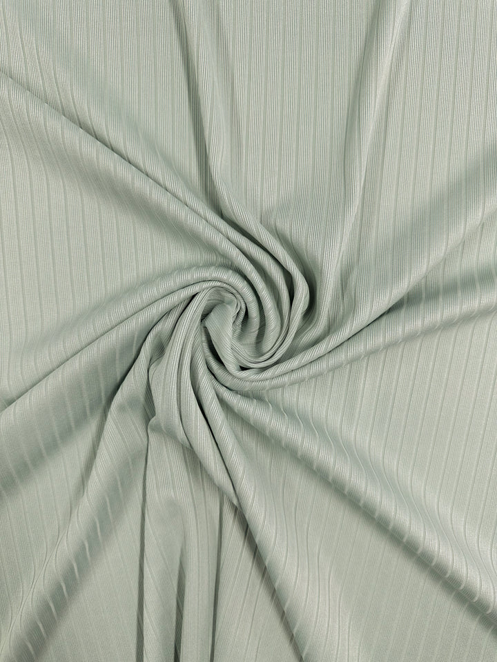 The Rib Knit - Murmur by Super Cheap Fabrics is a light green fabric with thin vertical lines, arranged in a spiral pattern at the center, creating soft folds and texture that showcase the allure of this medium-weight rib knit fabric.