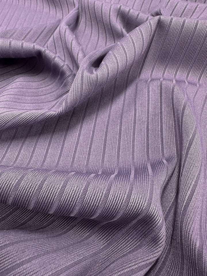 A close-up of folded Grape Compote fabric from Super Cheap Fabrics, featuring a ribbed texture with medium weight. The 170cm wide rib knit displays parallel lines for a dynamic look, while the stretch fabric offers flexibility.